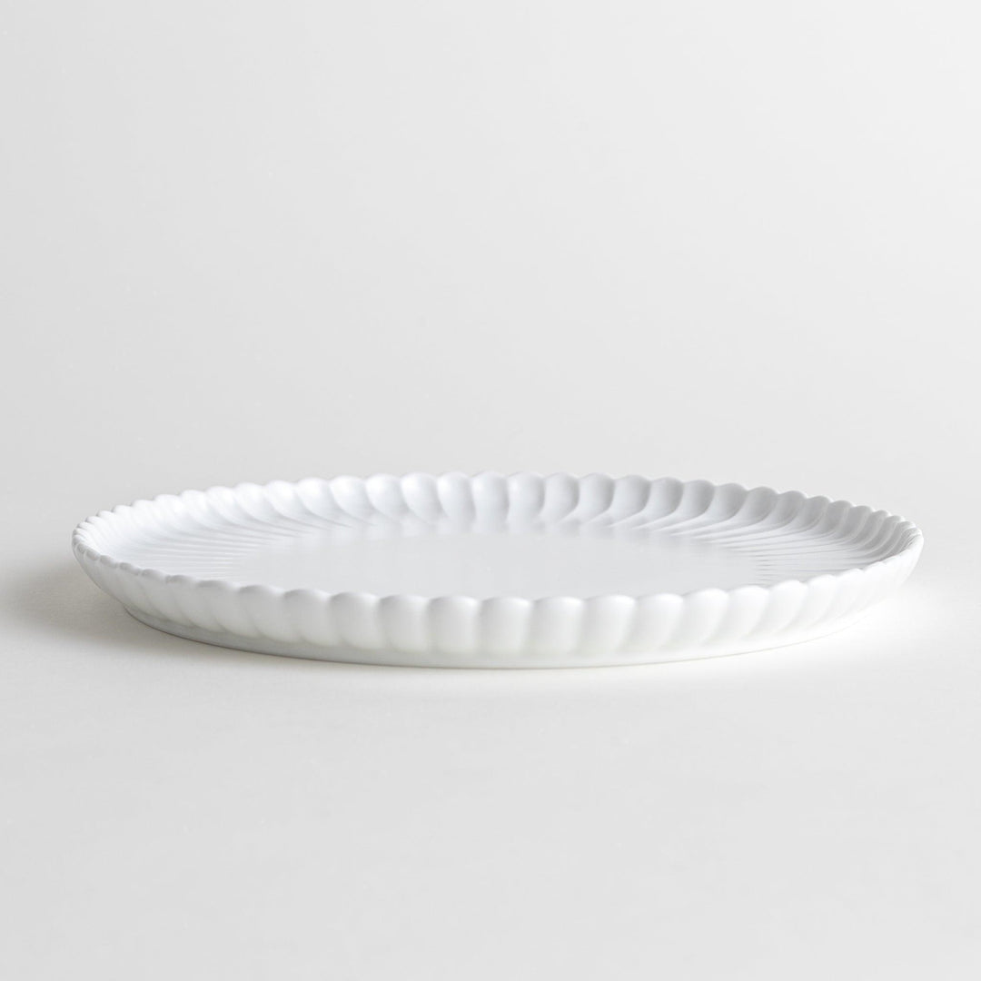 A white ceramic salad plate with a scalloped design with raised edges.