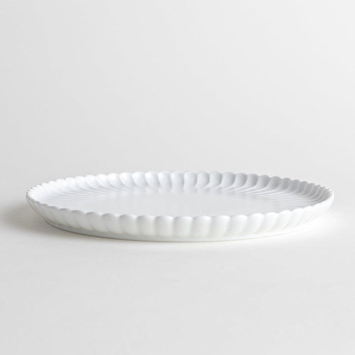 A white ceramic salad plate with a scalloped design with raised edges.