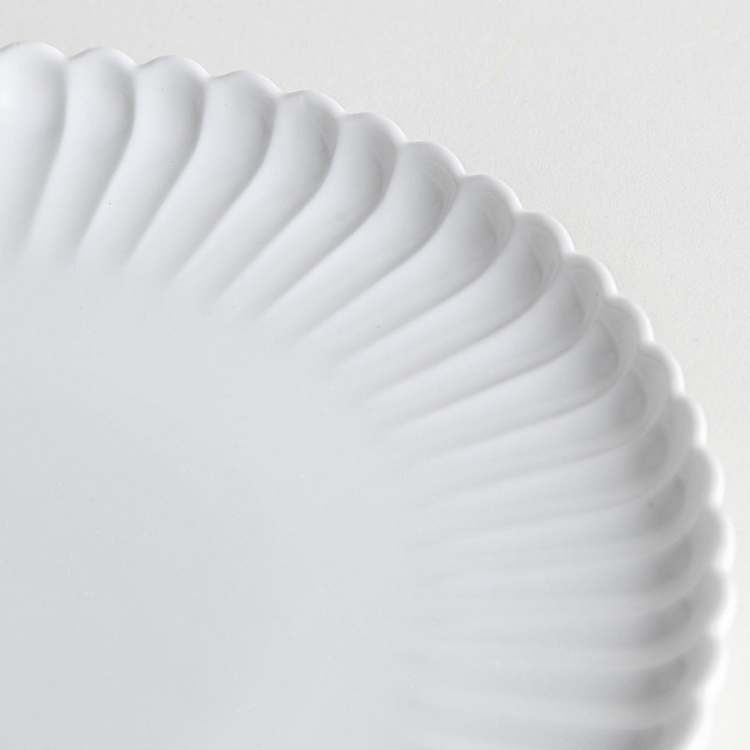 A white ceramic salad plate with a scalloped design with raised edges.