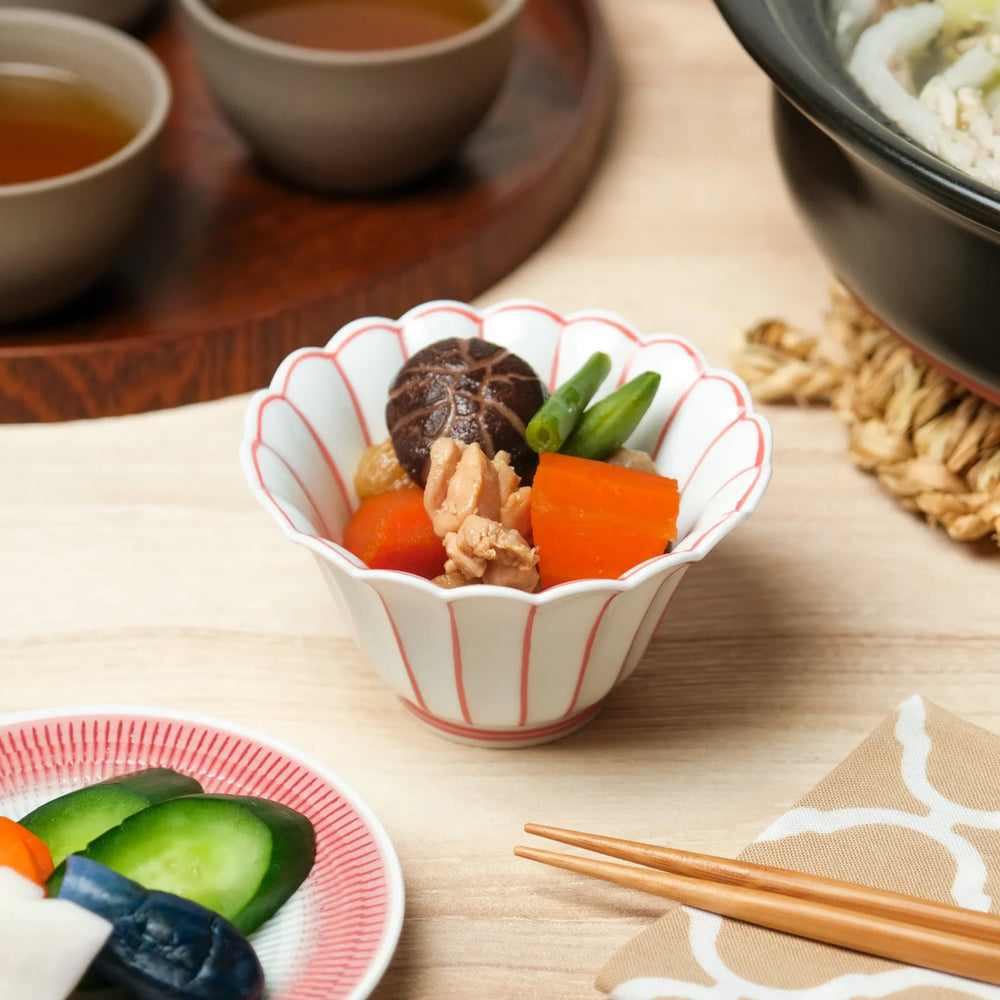 White scalloped Japanese bowl with red lines holding simmered vegetables carrot shiitake green beans and chicken.