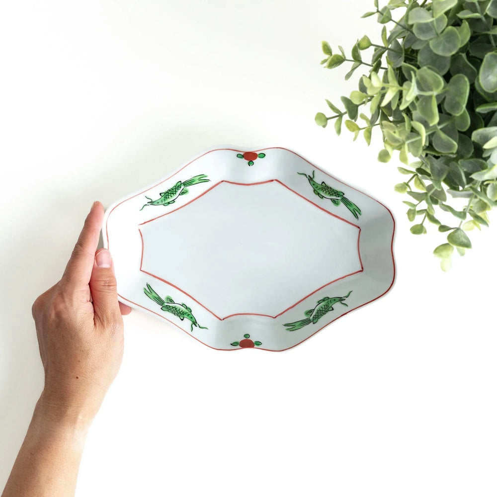 An irregularly shaped porcelain dish featuring hand-painted designs of fish and plants.