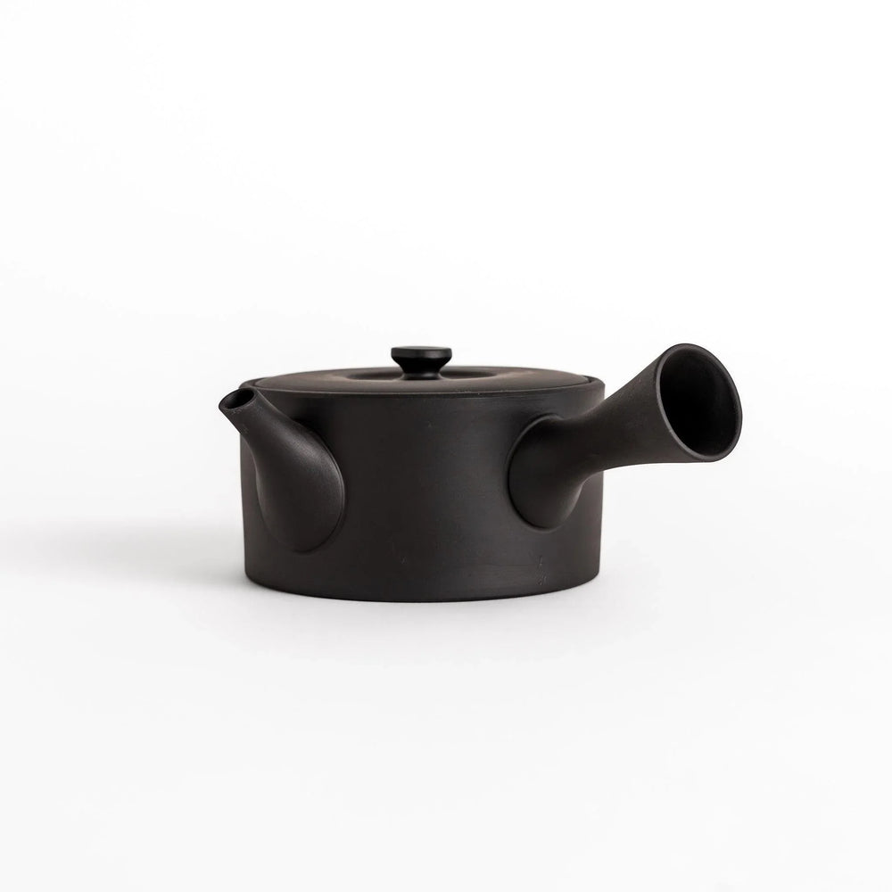 Minimalist black teapot with horizontal spout and handle textured ceramic body for refined experience.