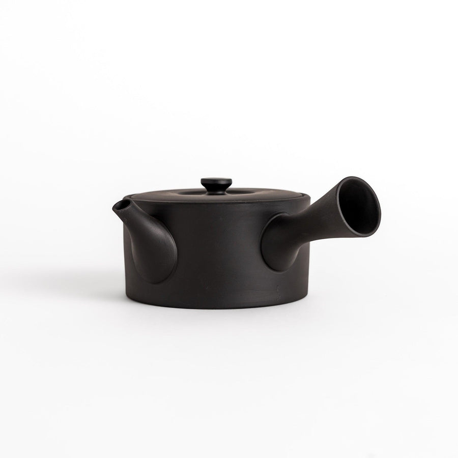 Minimalist black teapot with horizontal spout and handle textured ceramic body for refined experience.