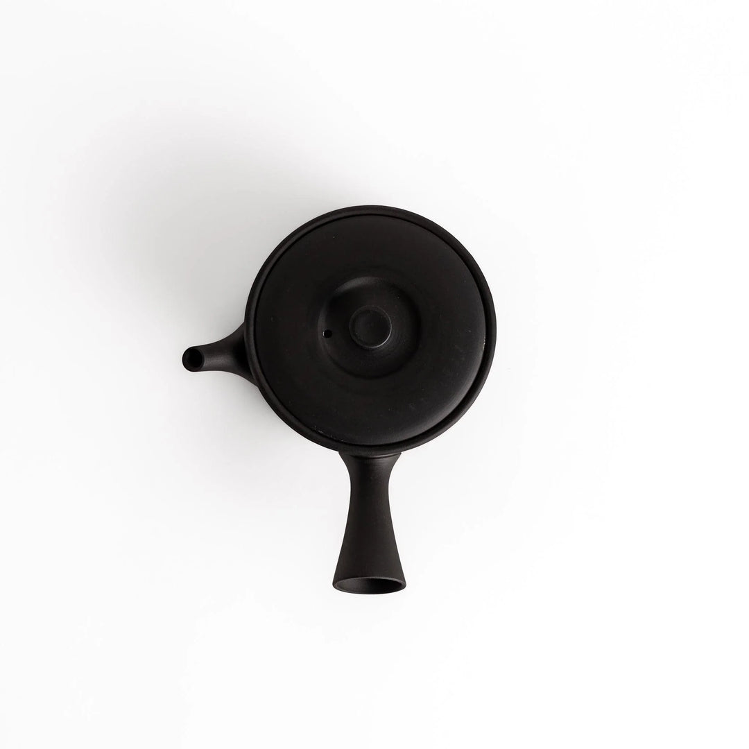 Minimalist black teapot with a horizontal spout and handle, crafted from textured ceramic, perfect for a refined tea experience.