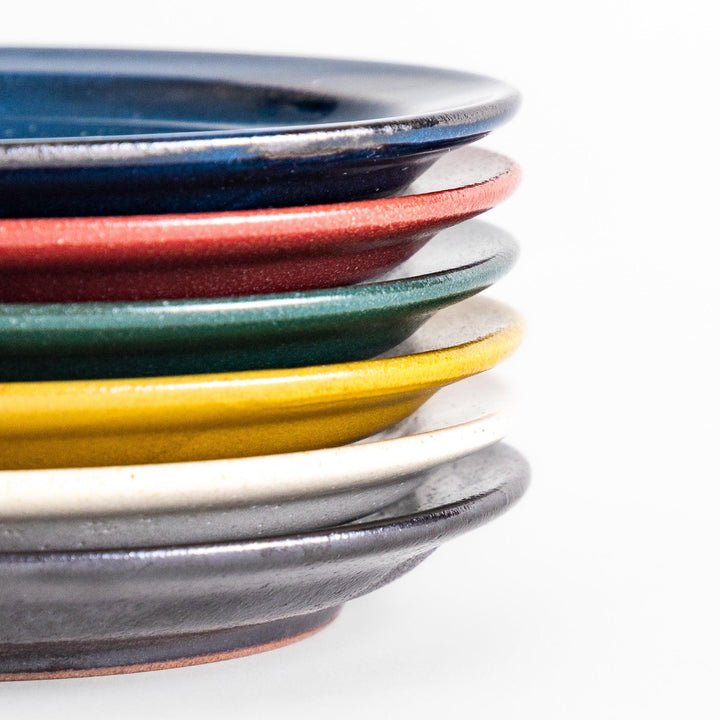 Stack of six colorful Japanese dessert plates in blue red green yellow white and black with glossy finish.