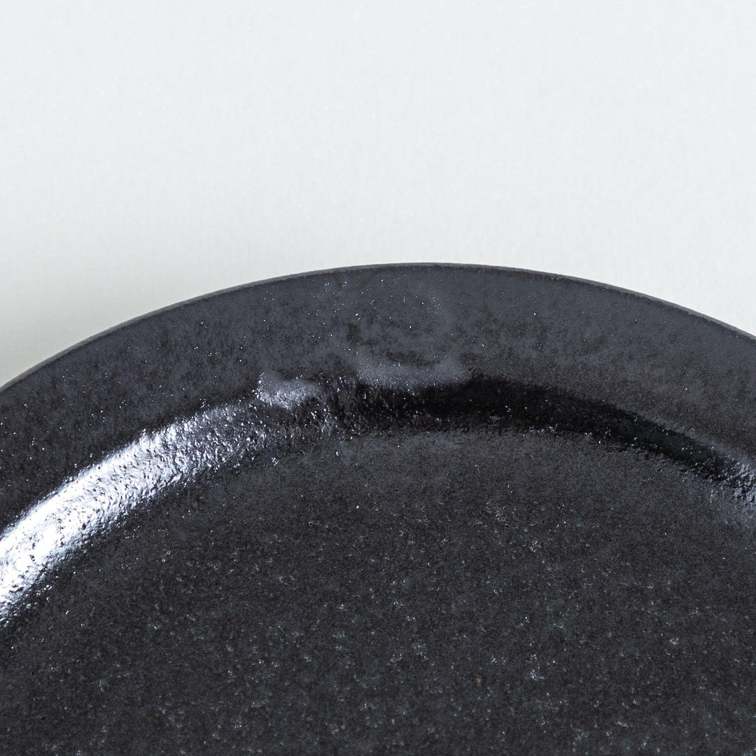 Deep black plate with a glossy surface, featuring handmade character seen in the uneven glaze along the rim.