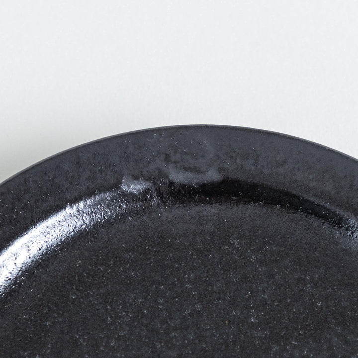 Deep black plate with a glossy surface, featuring handmade character seen in the uneven glaze along the rim.