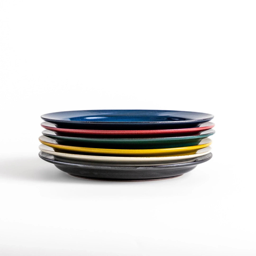Stacked Japanese ceramic dinner plates in blue, red, green, yellow, and black glazes showcasing modern craftsmanship.