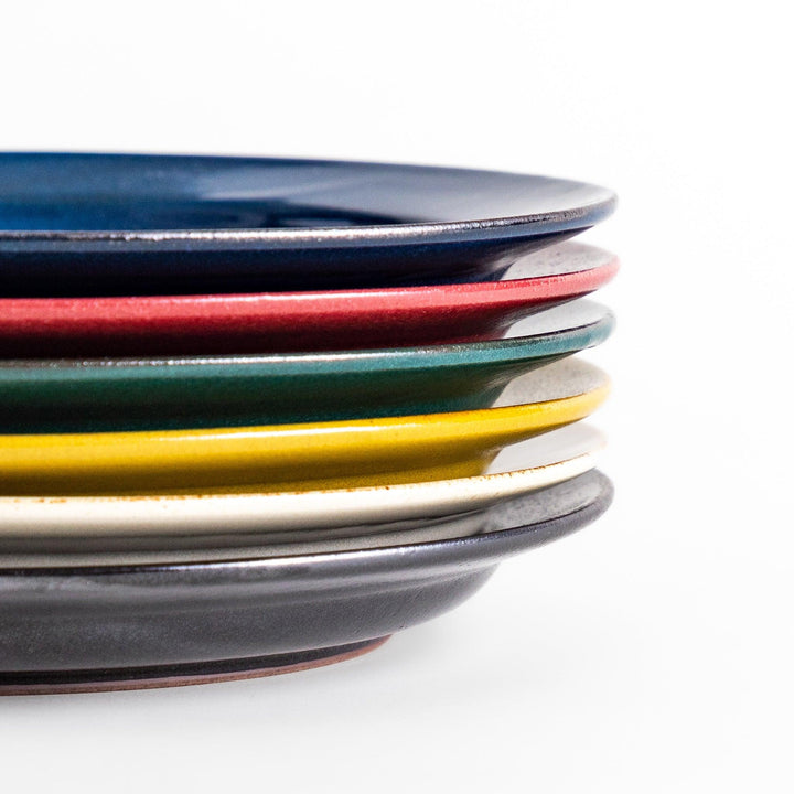 Stacked Japanese ceramic dinner plates in blue, red, green, yellow, and black glazes showcasing modern craftsmanship.