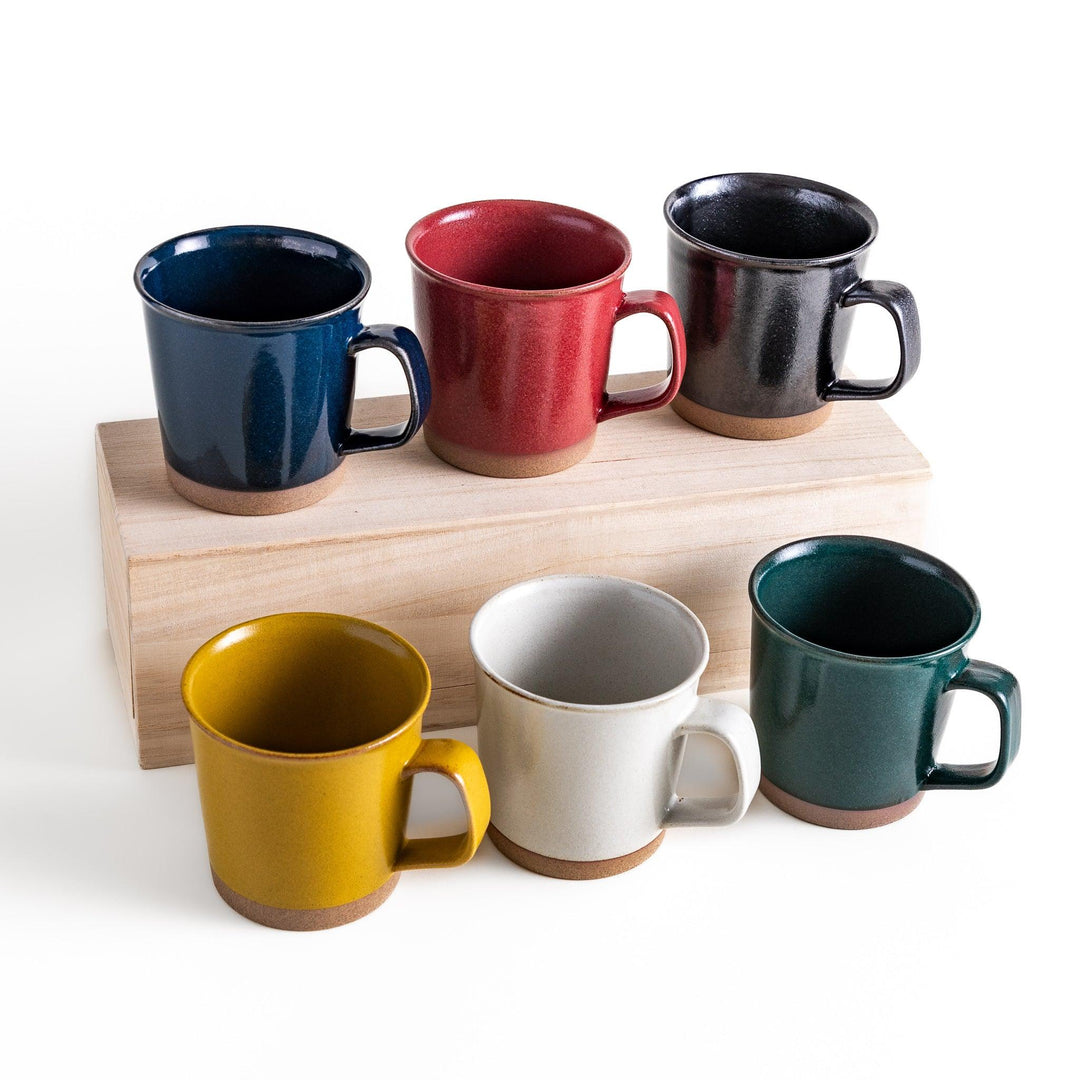 Colorful mug in blue red green yellow white or black with glossy finish and natural clay base on wooden block.
