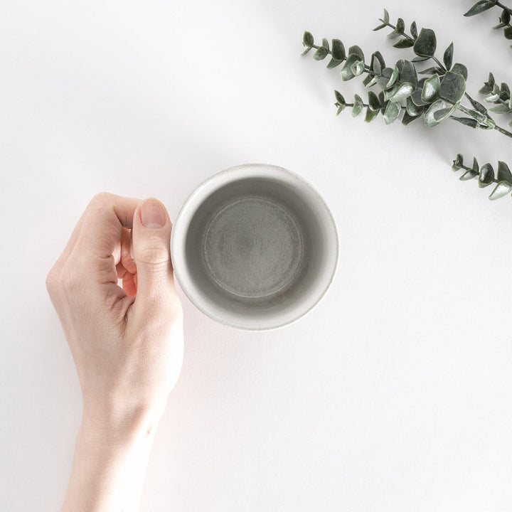 Top-down view of a white ceramic mug with a neutral-toned base, held in a hand, showcasing its smooth finish.