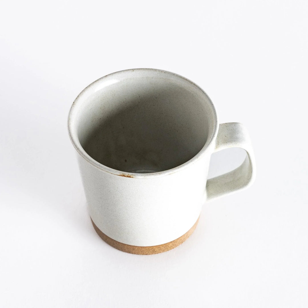 Slightly angled view of a white ceramic mug, highlighting its shape and neutral-toned base.