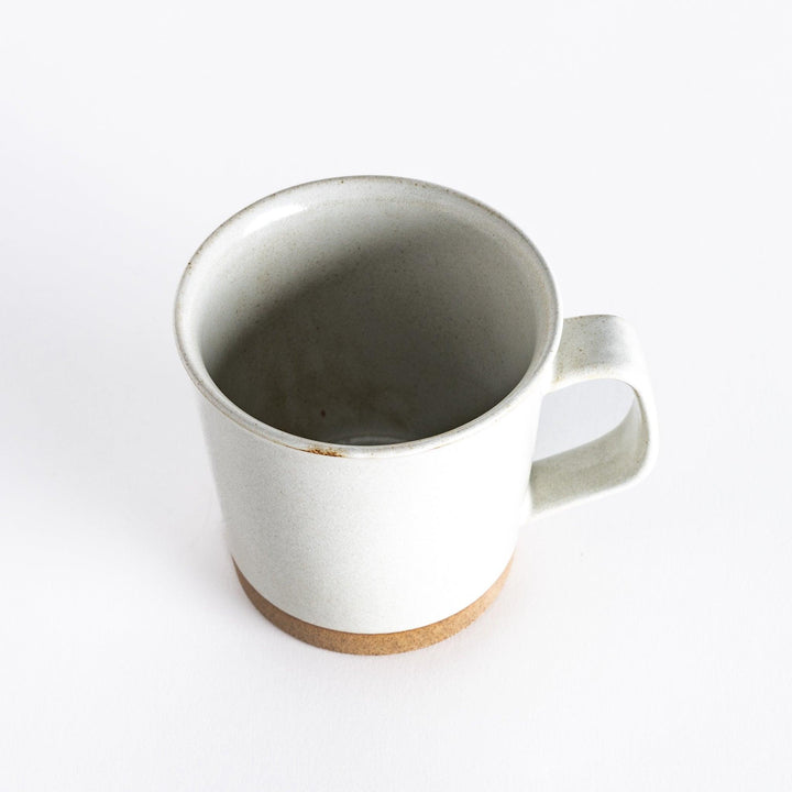 Slightly angled view of a white ceramic mug, highlighting its shape and neutral-toned base.
