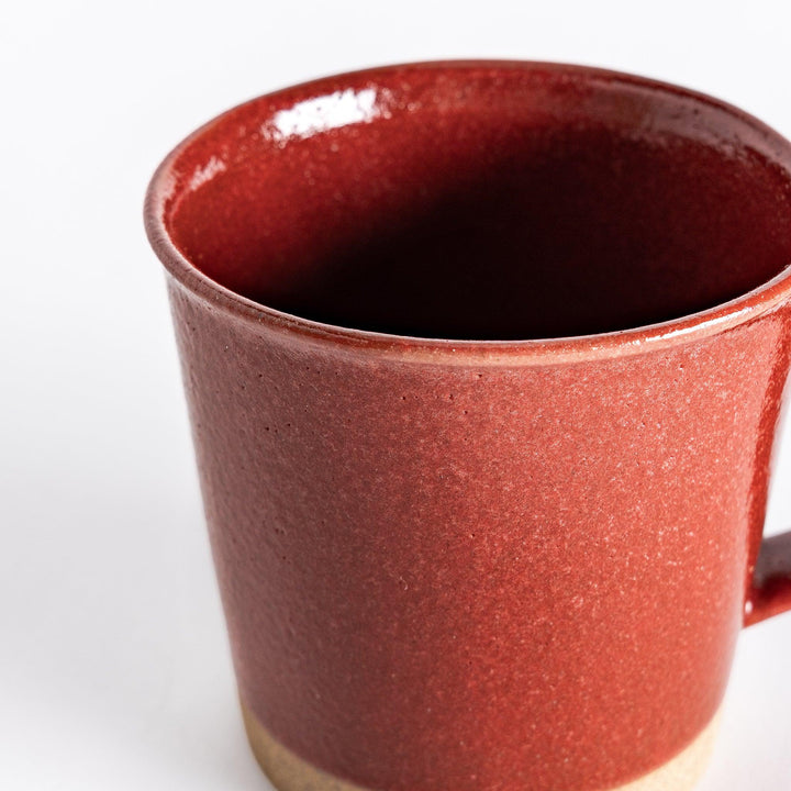 Close-up of a red ceramic mug focusing on the rich glossy red glaze and the subtle texture of the neutral-toned base.