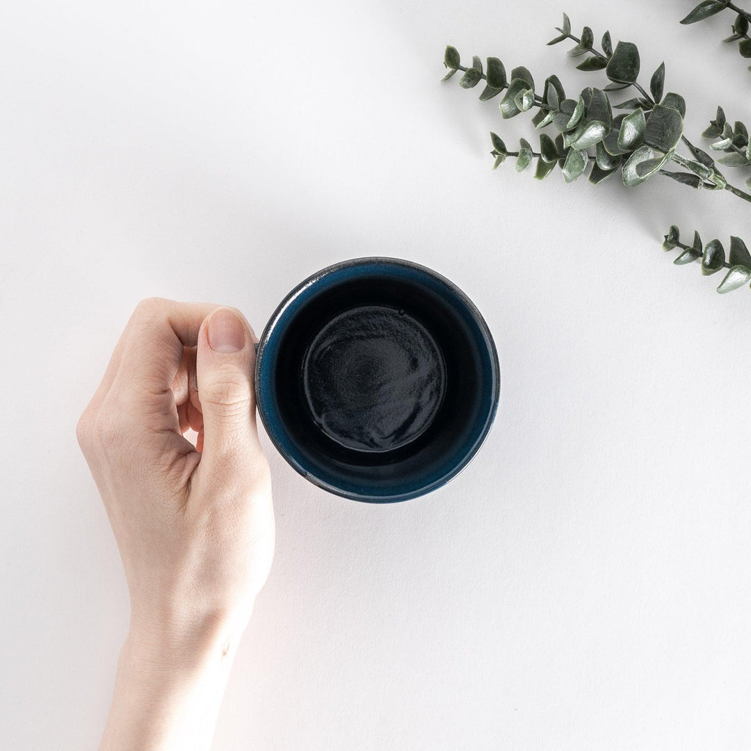 Top-down view of a blue ceramic mug held in hand, emphasizing its deep, round opening and smooth interior.