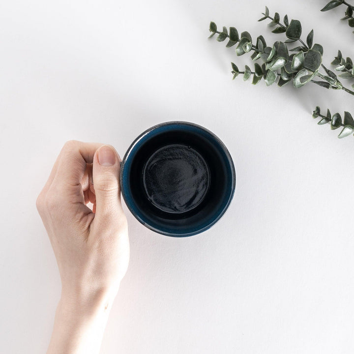 Top-down view of a blue ceramic mug held in hand, emphasizing its deep, round opening and smooth interior.