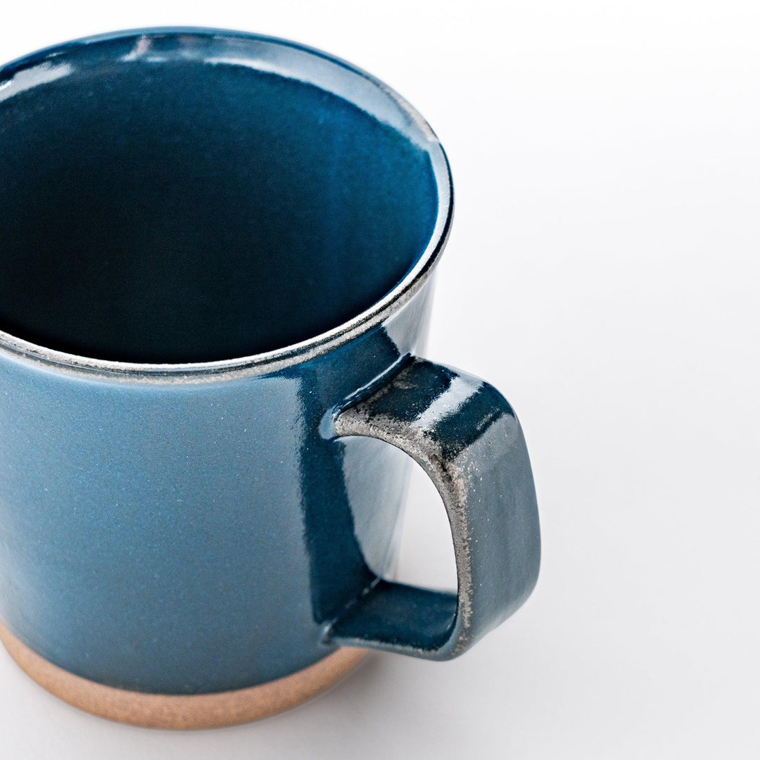 Close-up of a blue ceramic mug focusing on the glossy finish, smooth handle, and subtle texture on the neutral-toned base.