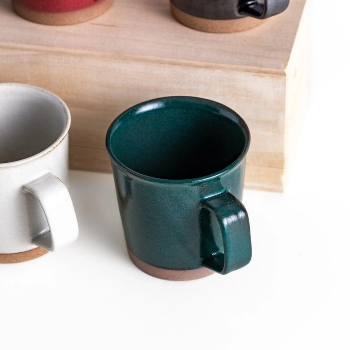 Colorful mug in blue red green yellow white or black with glossy finish and natural clay base on wooden block.
