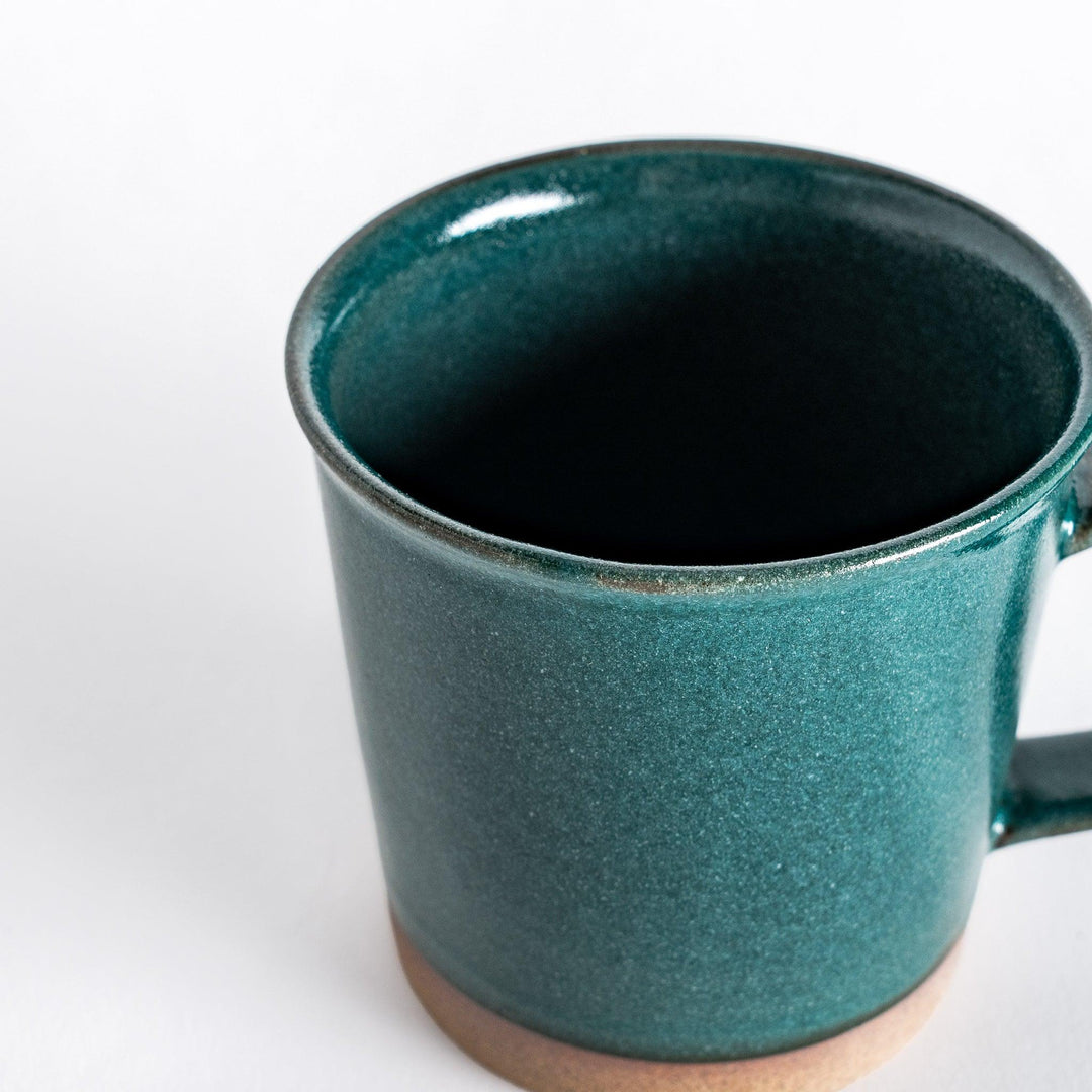 Close-up of a green ceramic mug highlighting the deep green glaze and the subtly textured neutral-toned base.