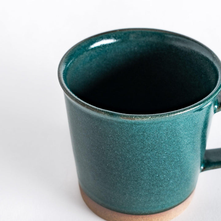 Close-up of a green ceramic mug highlighting the deep green glaze and the subtly textured neutral-toned base.