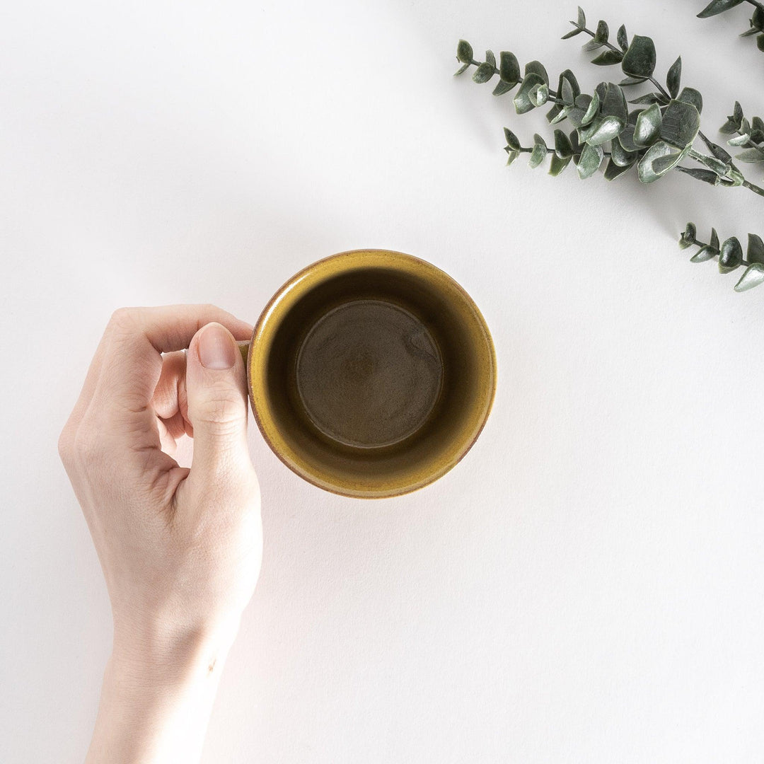 Top-down view of a yellow ceramic mug held in hand, showcasing its round opening and clean interior.