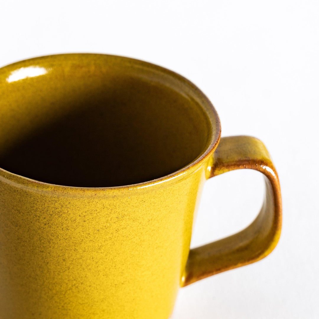 Close-up of a yellow ceramic mug focusing on the glossy yellow surface and the lightly textured base.