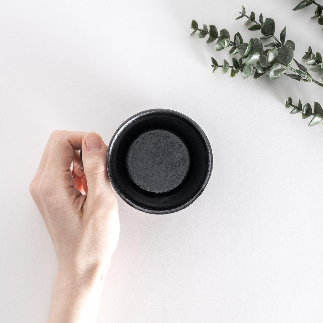 Top-down view of a black ceramic mug with a neutral-toned base, held in a hand, showing its smooth finish.