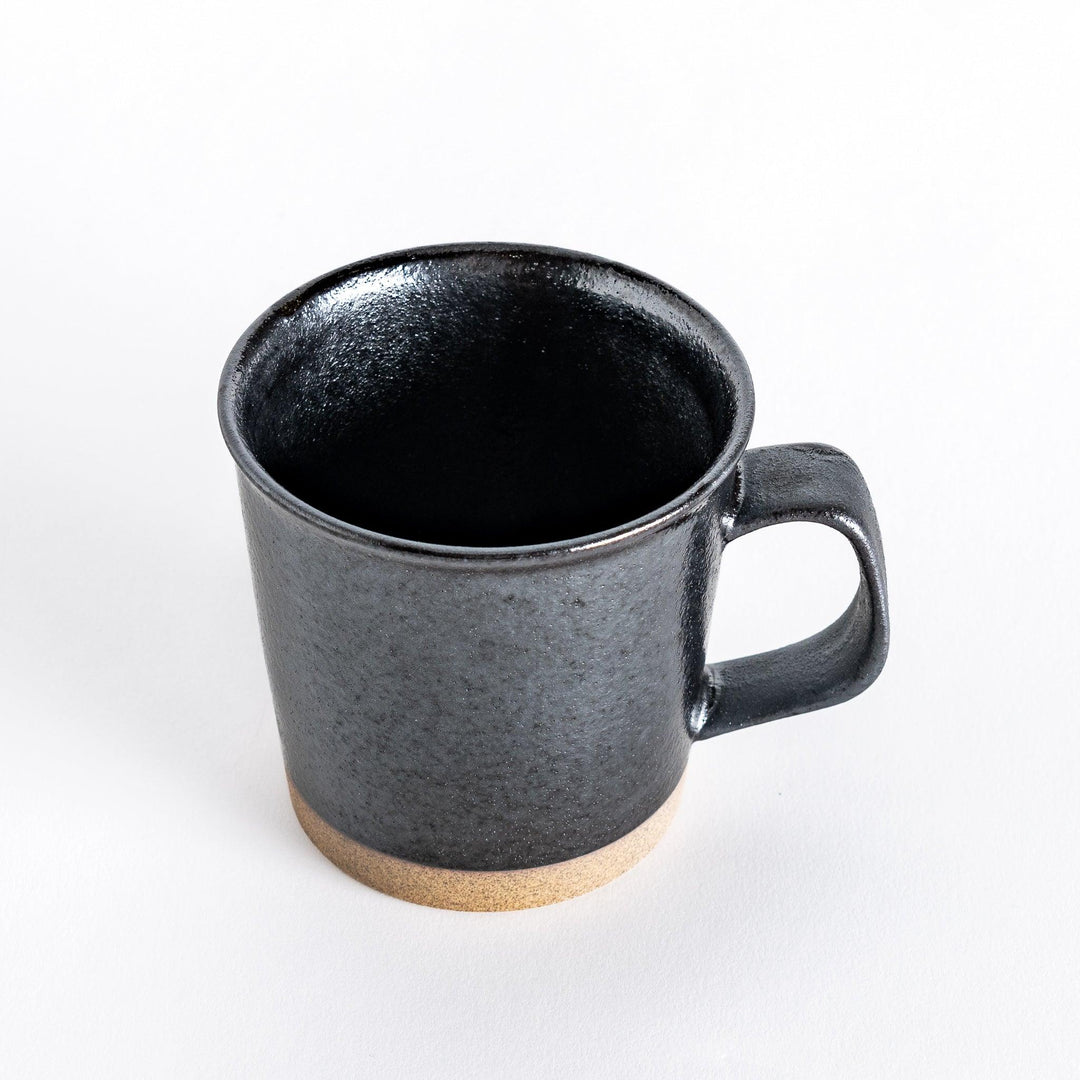 Slightly angled view of a black ceramic mug, showcasing its shape and neutral-toned base.