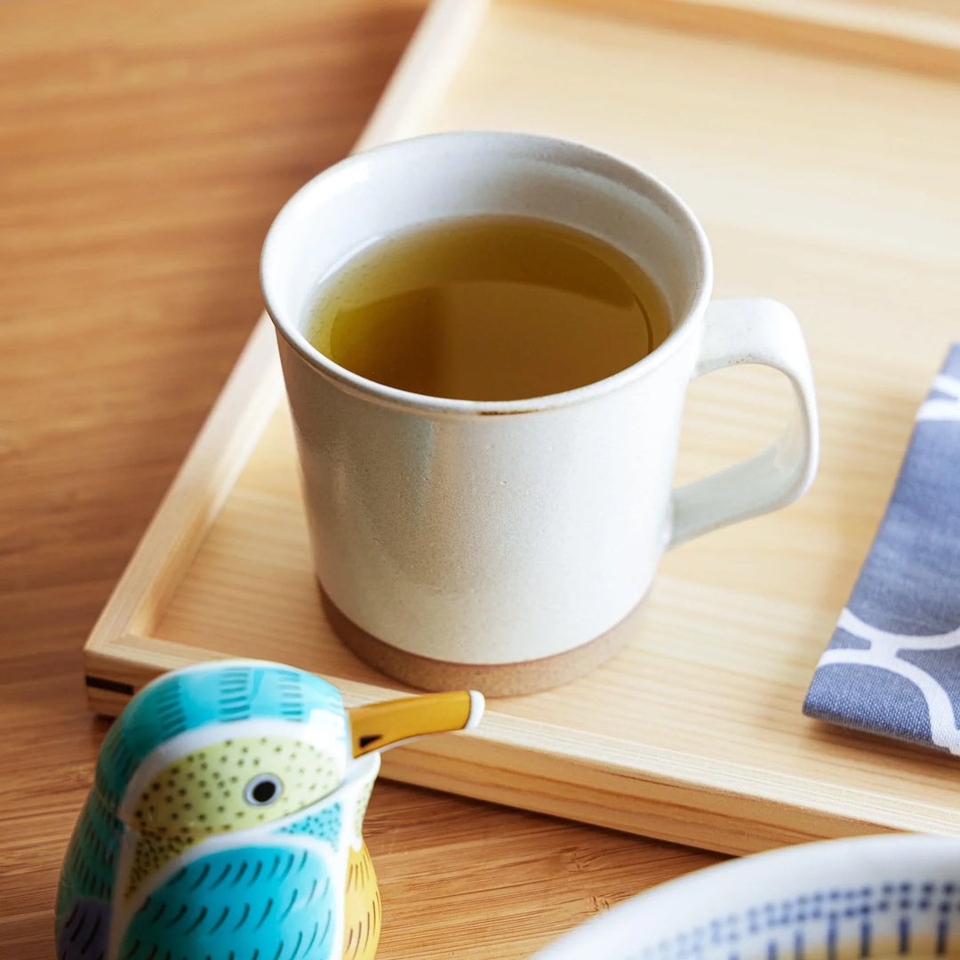 A simple white ceramic mug with a smooth matte finish and a brown base, filled with light amber tea.