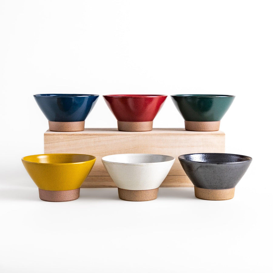 Set of six colorful Japanese rice bowls in blue red yellow white green and black with clay base.