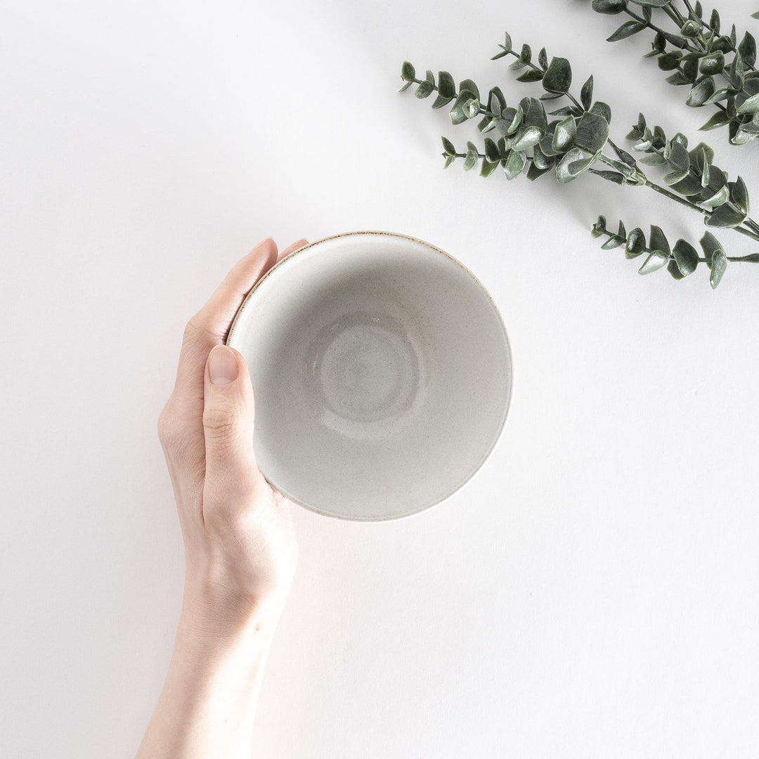 White ceramic rice bowl held by hand, captured from above to show its clean and smooth interior.