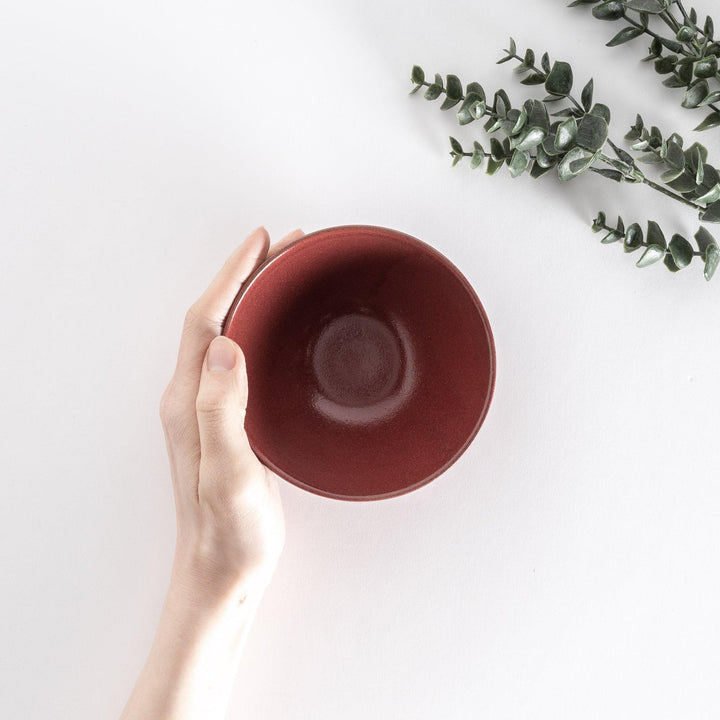 Red ceramic rice bowl held by hand, viewed from above to reveal its smooth and vibrant interior.