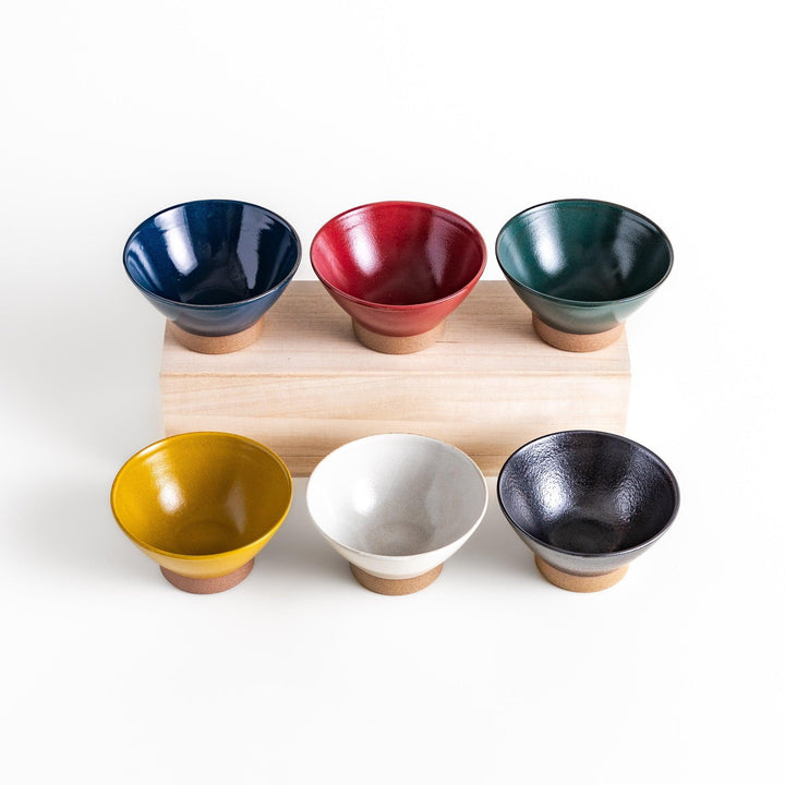 Set of six colorful Japanese rice bowls in blue red yellow white green and black with clay base.