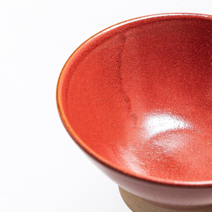 Close-up of the red ceramic rice bowl, focusing on its vivid color, smooth surface, and neutral-toned base.