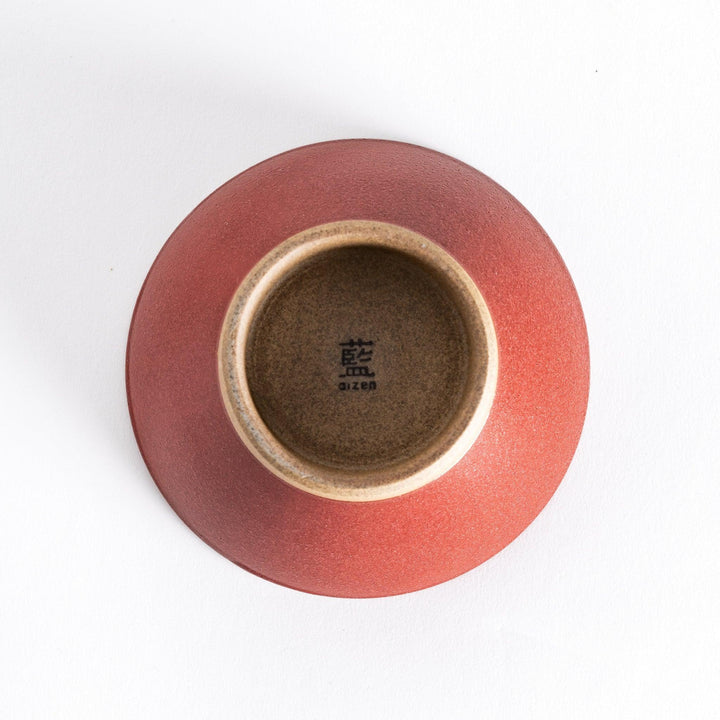 Bottom view of the red ceramic rice bowl, displaying its neutral-toned base and smooth curves.