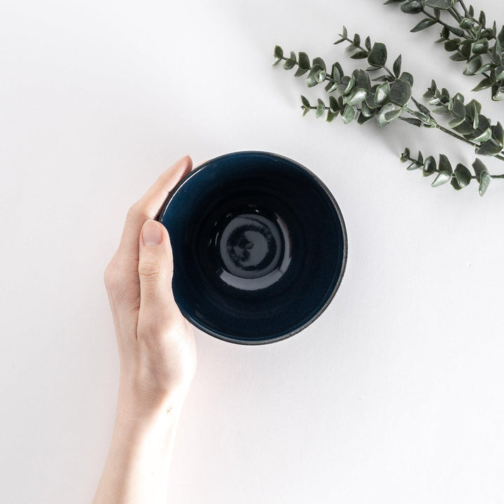 Blue ceramic rice bowl held by hand, viewed from directly above, showing its smooth and reflective interior.