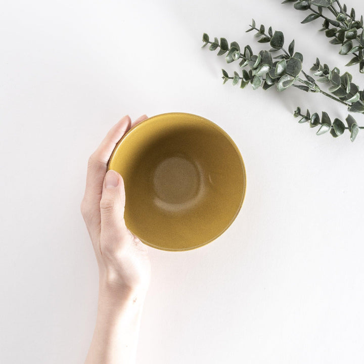Yellow ceramic rice bowl held by hand, viewed from directly above to reveal its vibrant yellow interior.