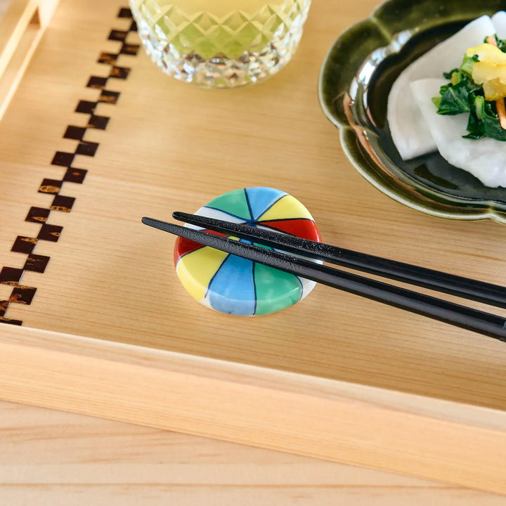 A colorful round chopstick rest with a segmented rainbow pattern, holding black chopsticks.