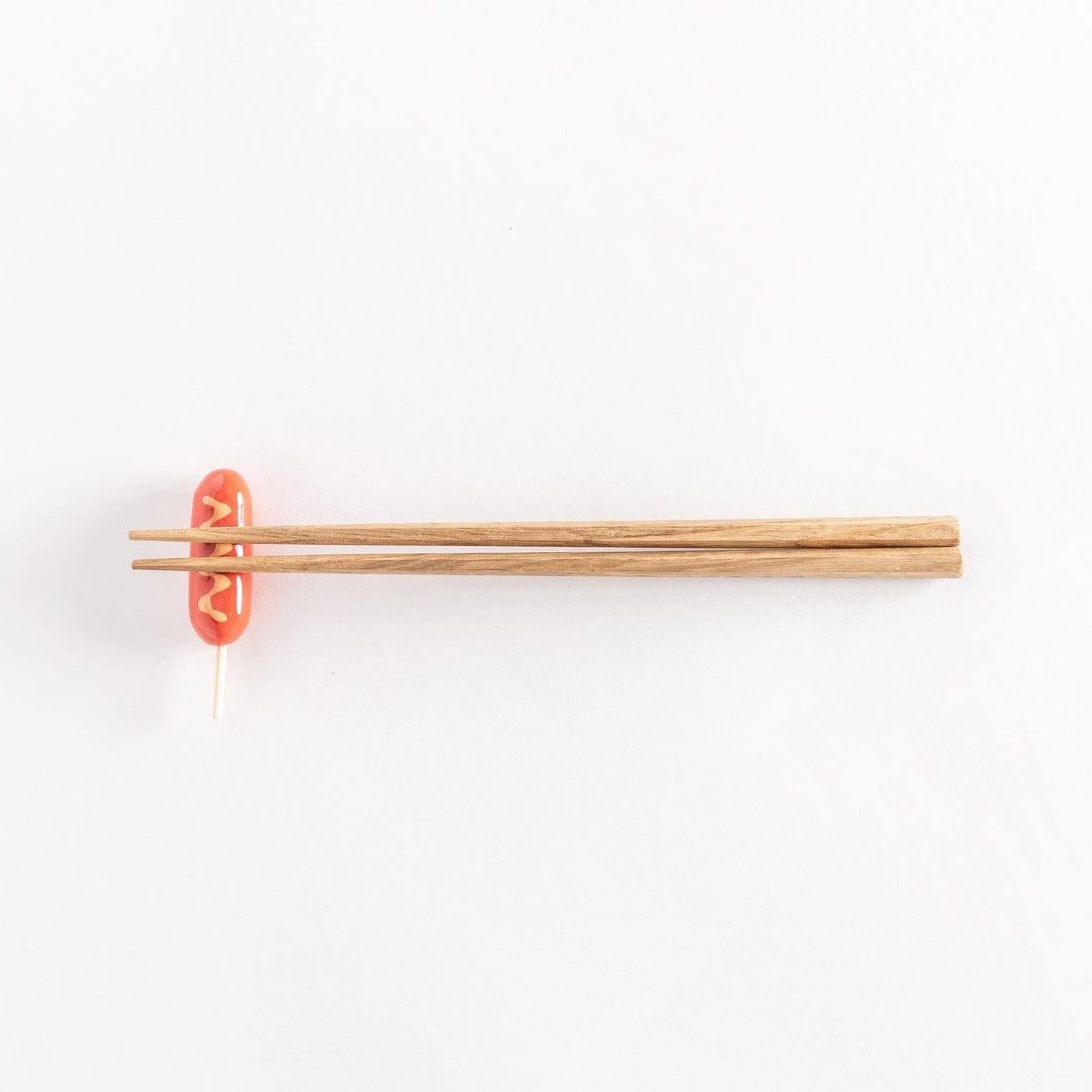 Full view of a corn dog chopsticks rest with wooden chopsticks resting on top.