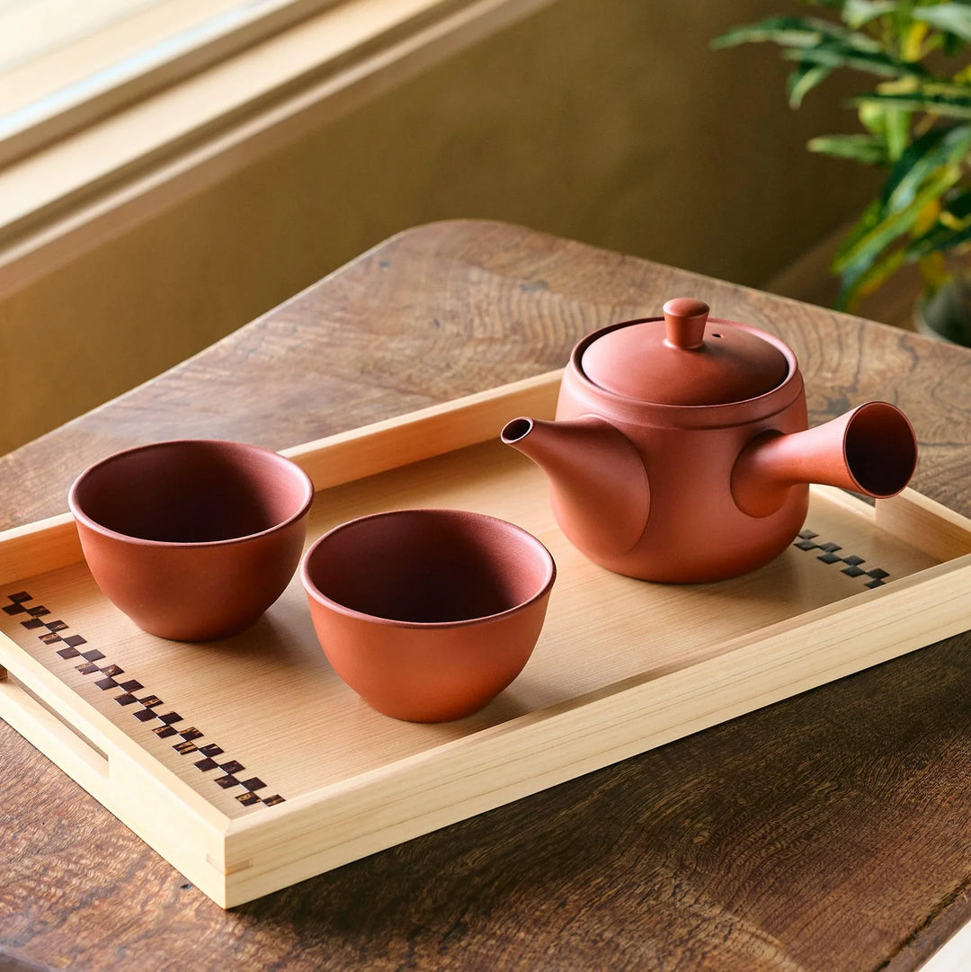 Traditional Japanese tea set with a reddish-brown clay teapot and two matching cups on a wooden tray