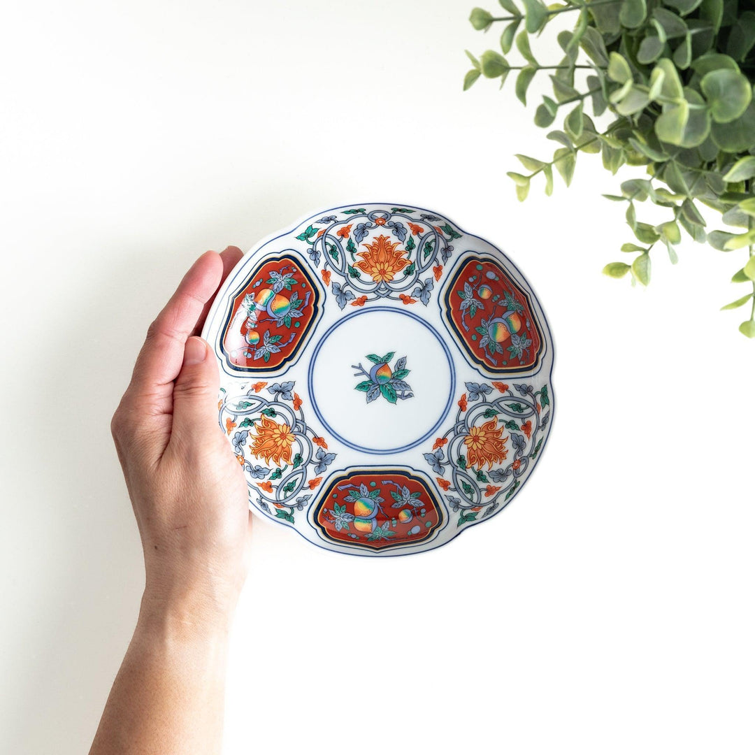 Round dessert plate with floral center and scalloped rim featuring red green and gold intricate patterns.