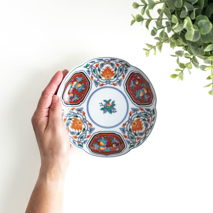 Round dessert plate with floral center and scalloped rim featuring red green and gold intricate patterns.