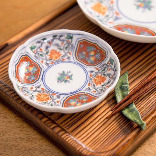 Japanese porcelain sauce dish with red and blue floral patterns and gold accents, displayed on a wooden tray with chopsticks