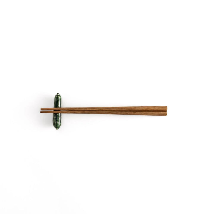 Glossy green ceramic cucumber chopstick rest with textured details adding playful accent to dining table.