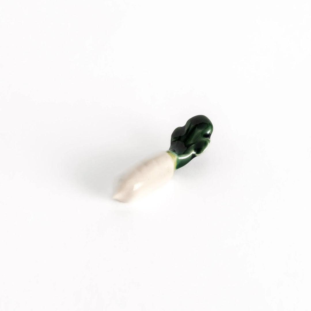 Glossy ceramic daikon radish chopstick rest with green top and white body showing realistic vegetable look.