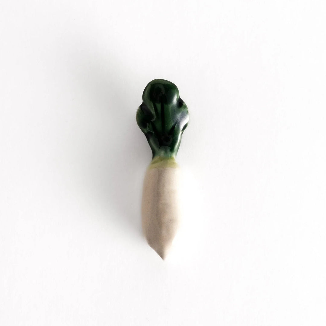 Glossy ceramic daikon radish chopstick rest with green top and white body showing realistic vegetable look.
