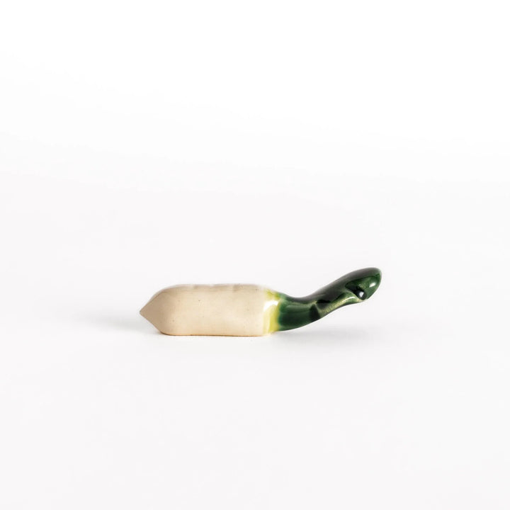 Glossy ceramic daikon radish chopstick rest with green top and white body showing realistic vegetable look.