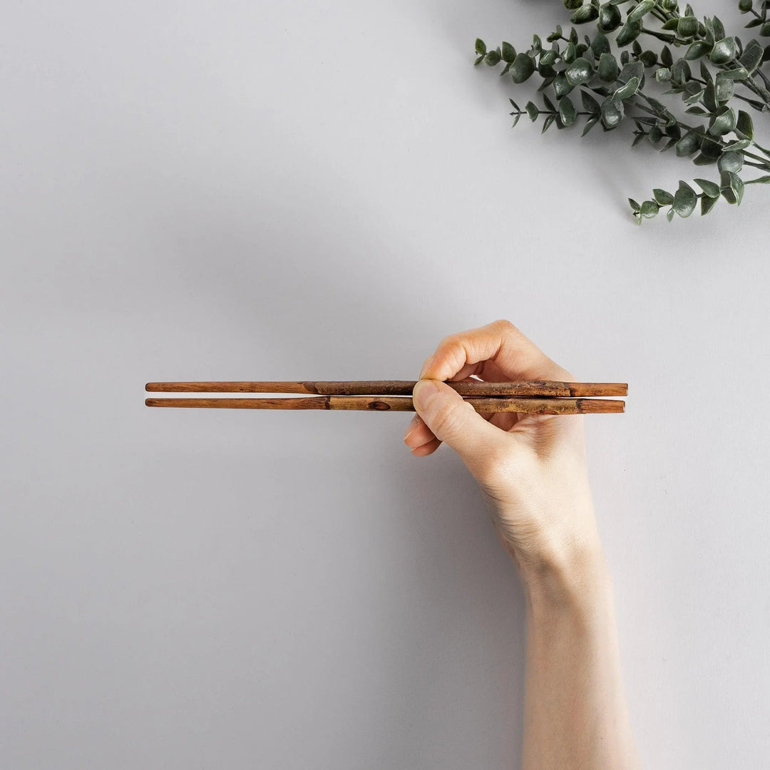 Hand holding Dark Plum Branch Chopsticks, demonstrating their size and unique, organic design.