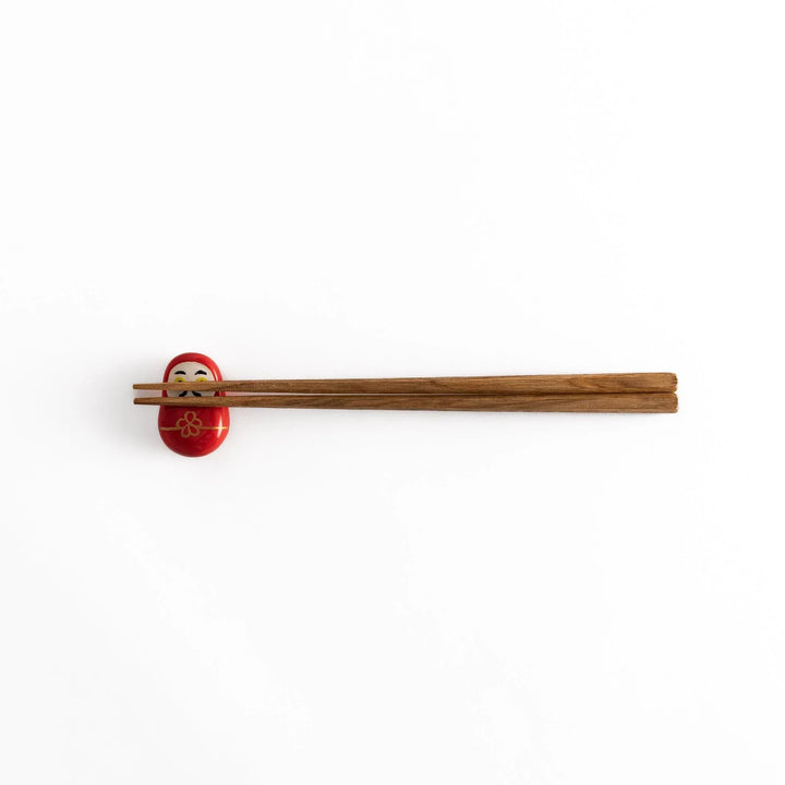 A distant view of chopsticks placed on the red daruma chopstick rest, showcasing its overall design and vibrant colors.