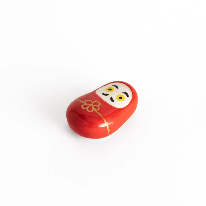 A slightly angled view of the daruma chopstick rest, emphasizing its rounded shape, gold accents, and detailed features.